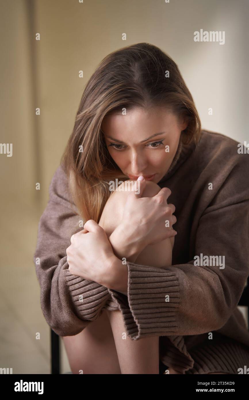Worried woman hugging knee sitting at home Stock Photo - Alamy