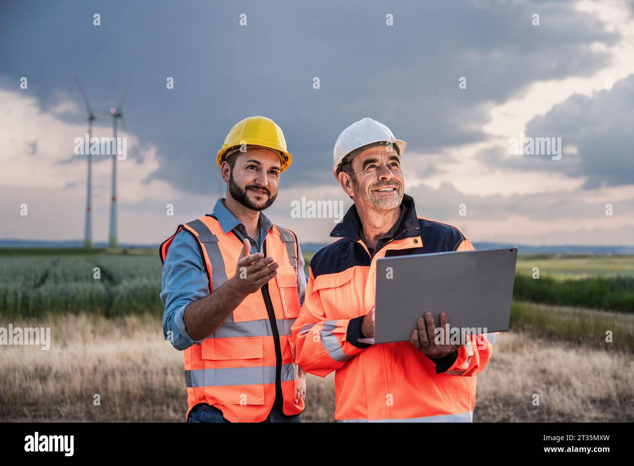 Smiling engineers working with laptop at wind farm Stock Photo