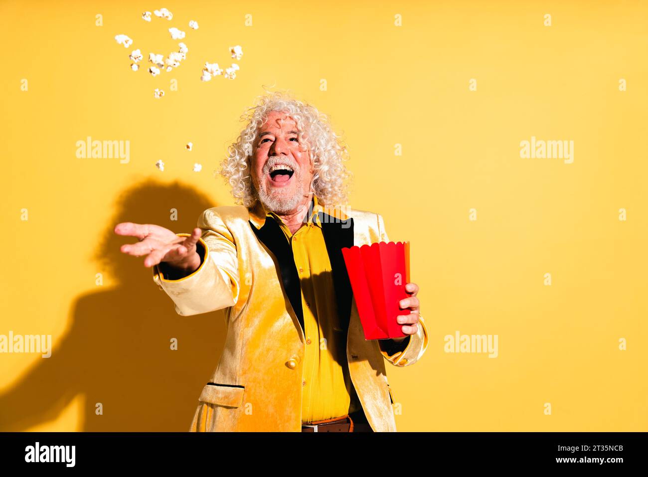 Cheerful senior man catching popcorn against yellow background Stock Photo