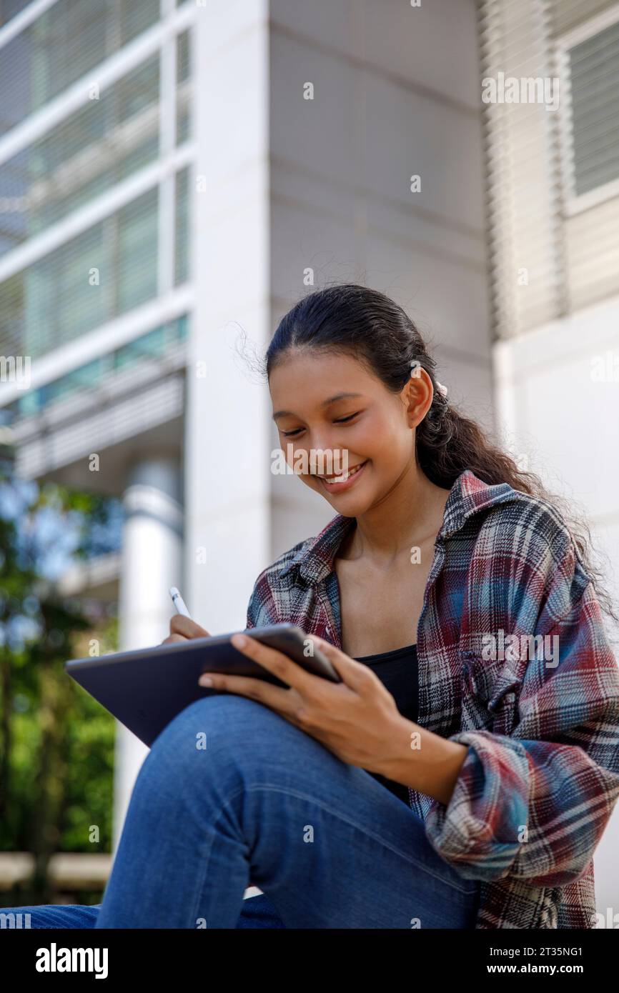 Smiling student using tablet PC sitting outside university Stock Photo