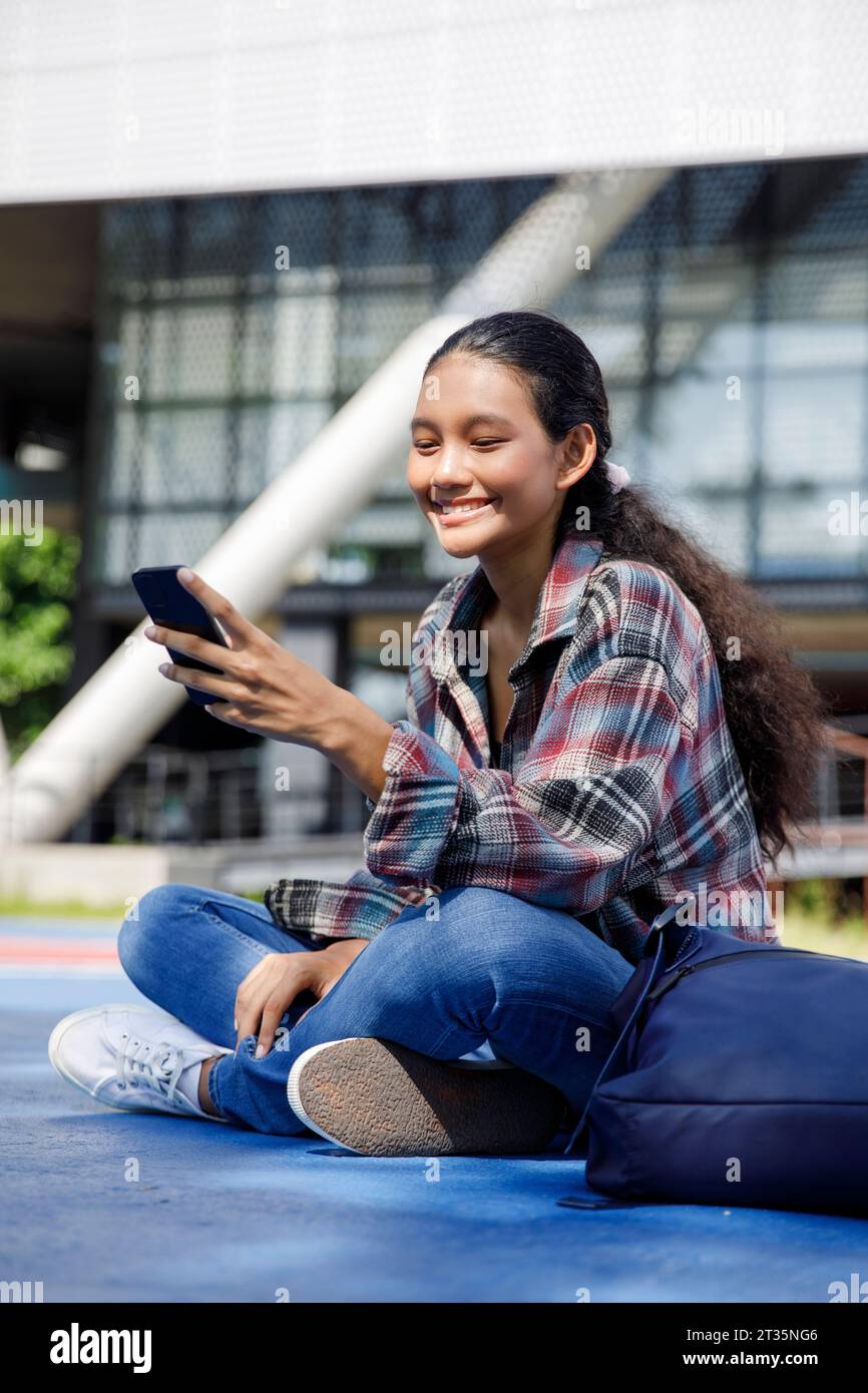 Smiling student using smart phone in front of university Stock Photo