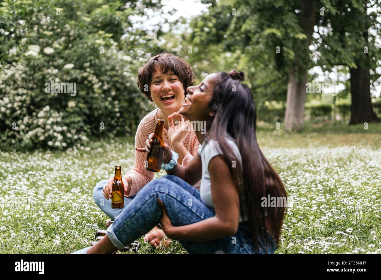Young friends holding beer and laughing at park Stock Photo