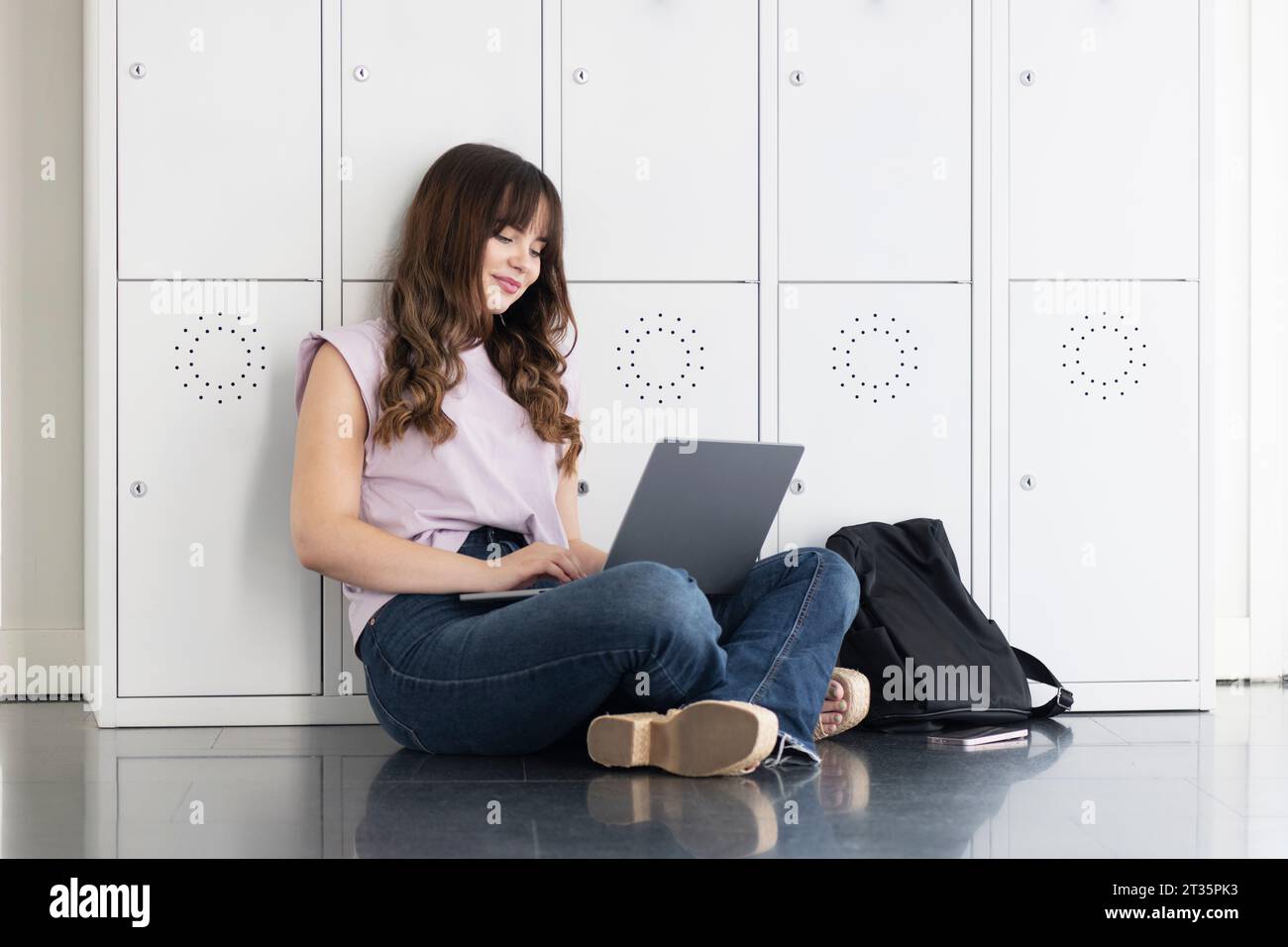 Smiling student using laptop and sitting on floor Stock Photo