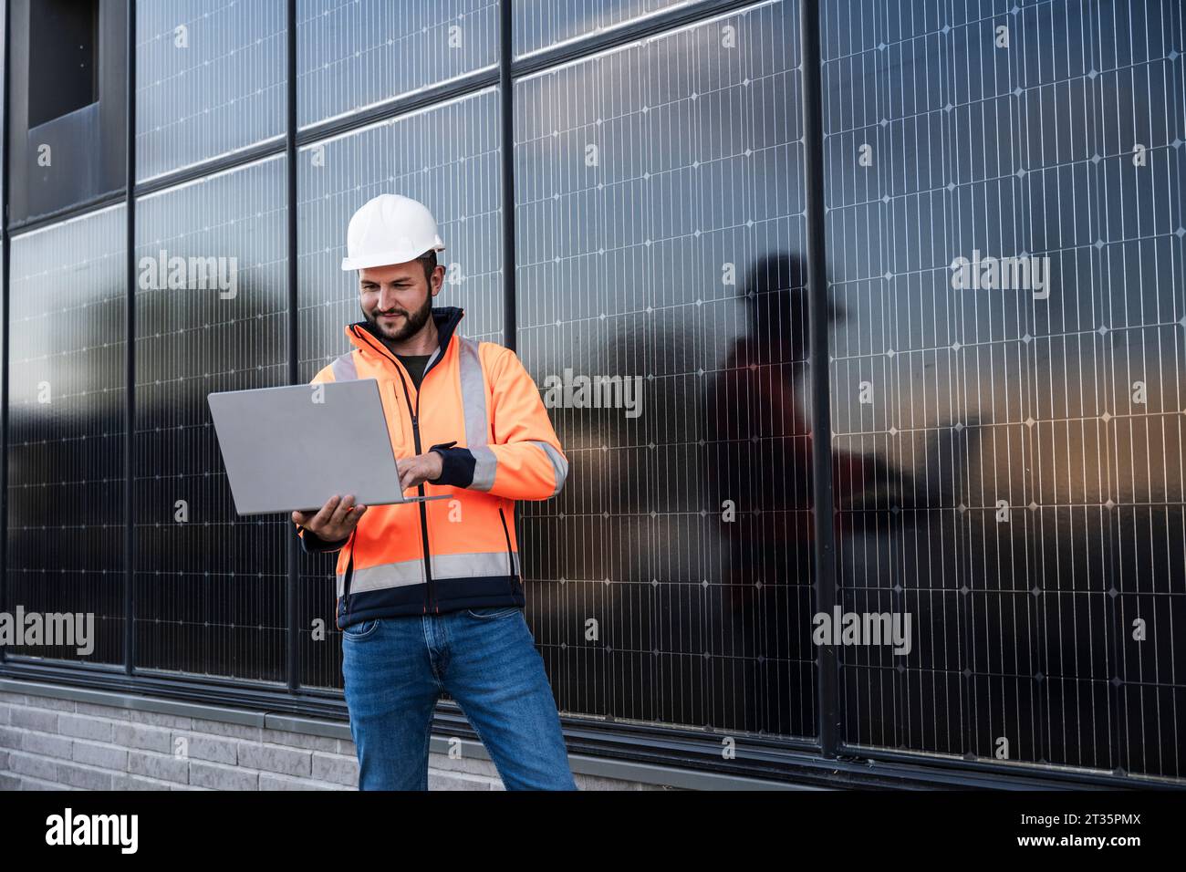 Smiling engineer using laptop standing near solar panels Stock Photo