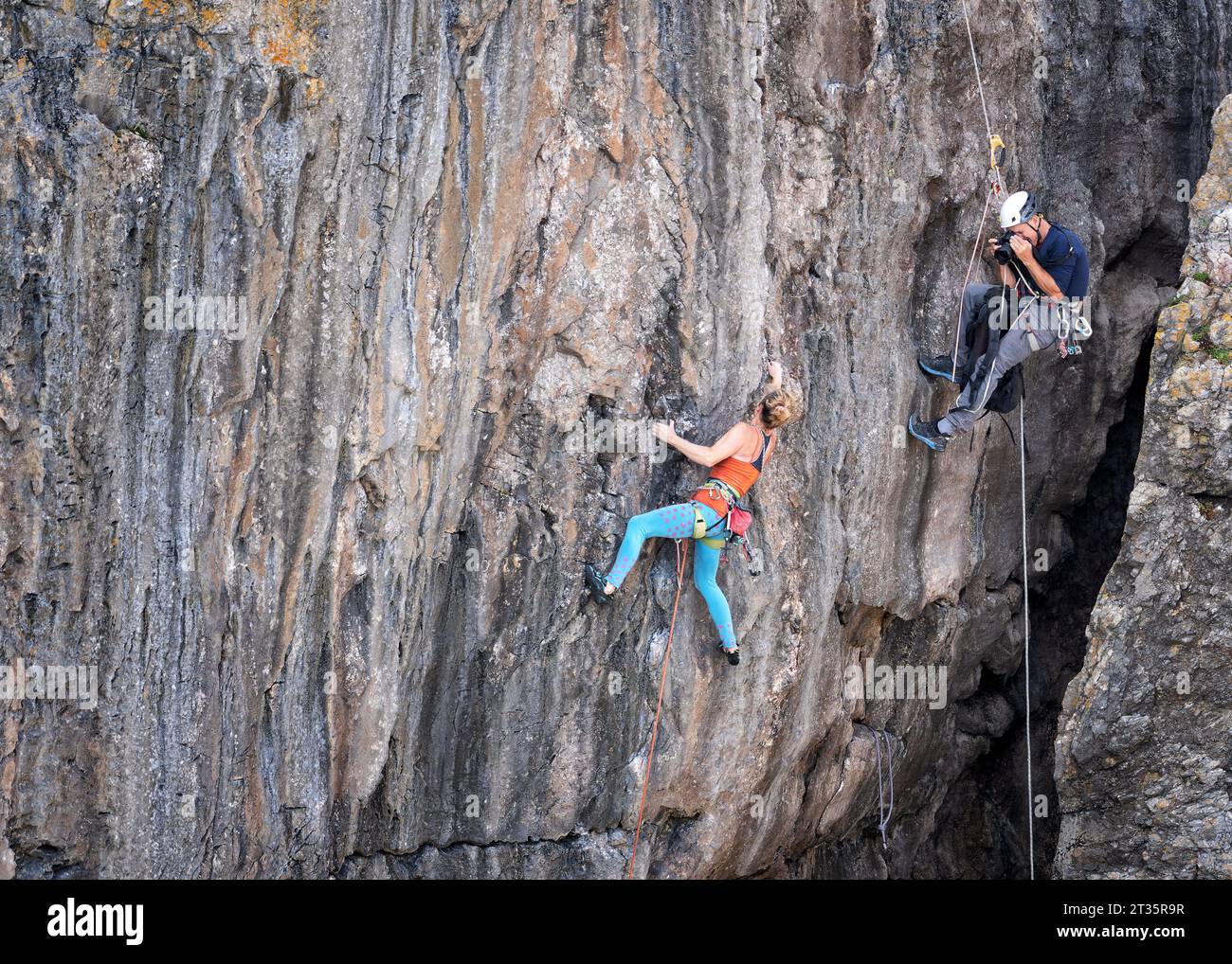 Man photographing woman climbing mountain with rope Stock Photo