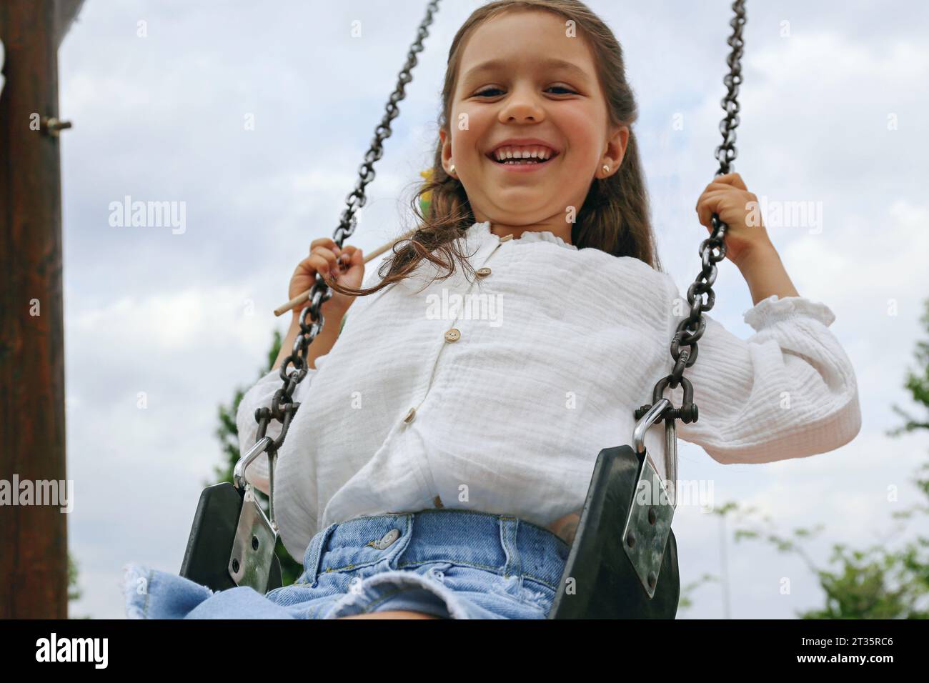Girl swinging on swing in front of sky Stock Photo