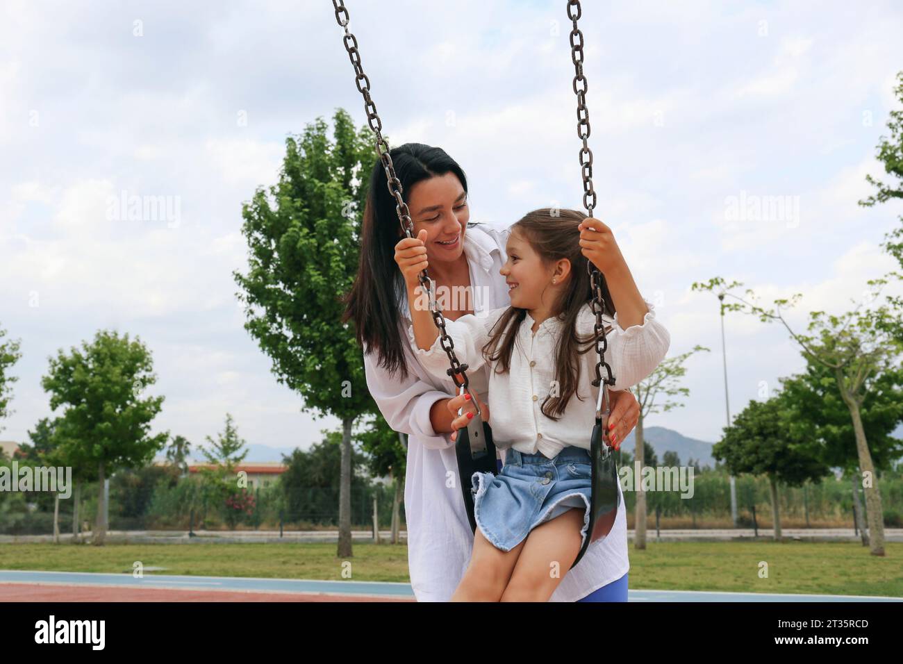 Happy mother spending time with daughter sitting on swing in park Stock Photo