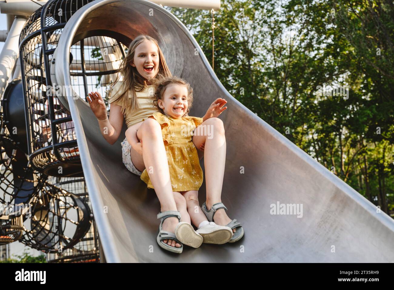 Happy siblings playing on slide at park Stock Photo