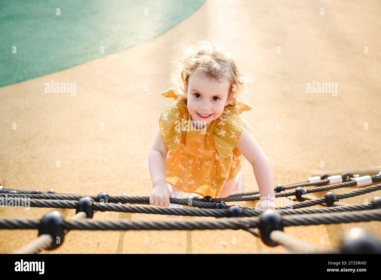 Smiling girl climbing on rope at jungle gym Stock Photo