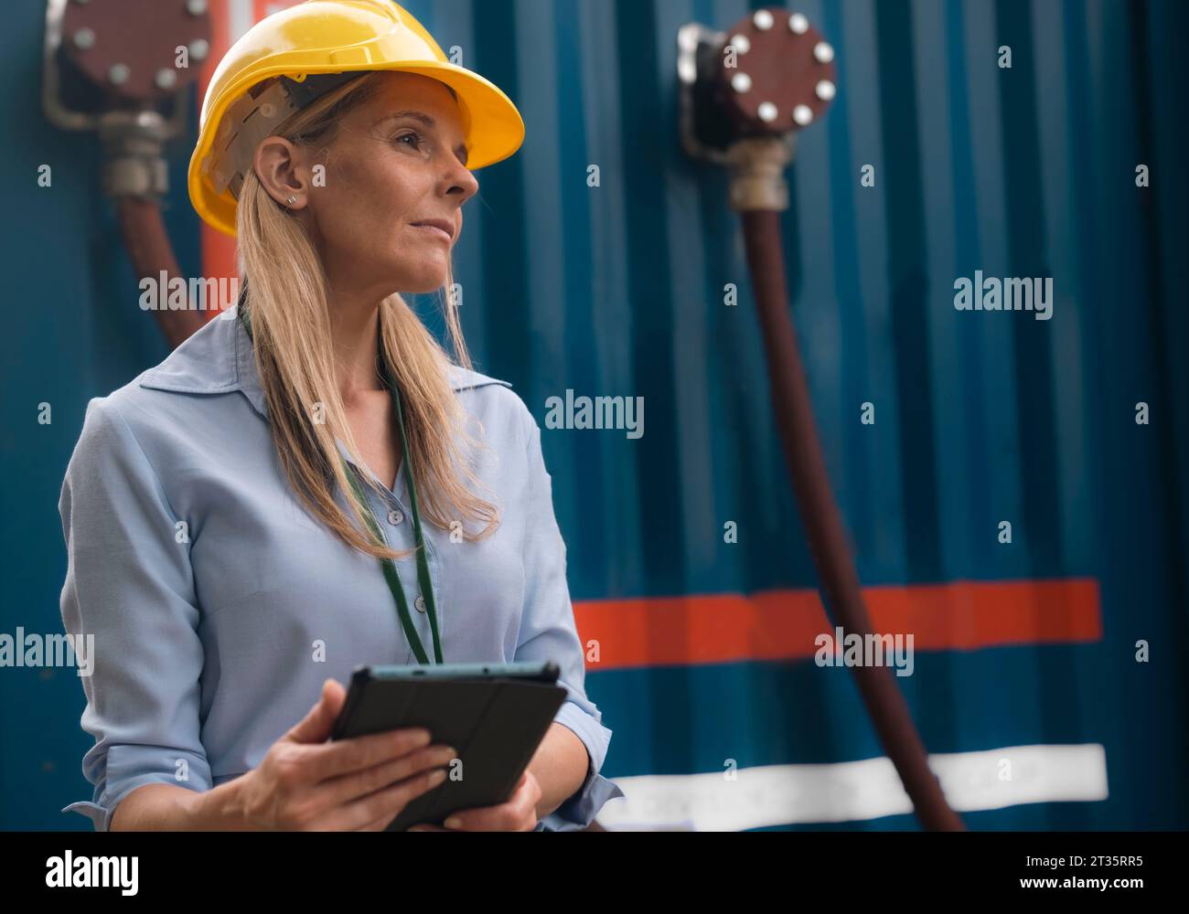 Contemplative engineer wearing hardhat holding tablet PC Stock Photo