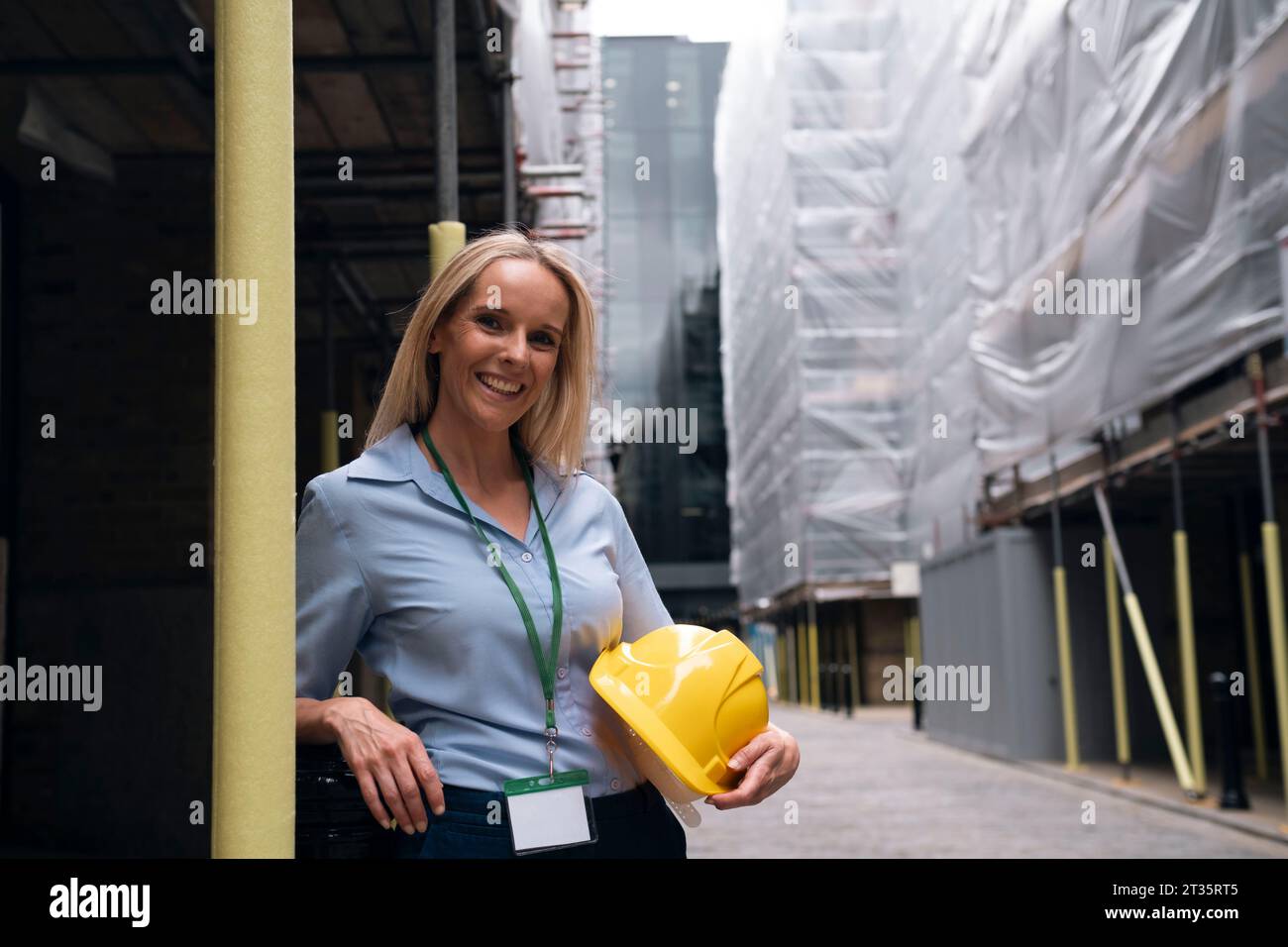 Happy engineer leaning on pole at construction site Stock Photo