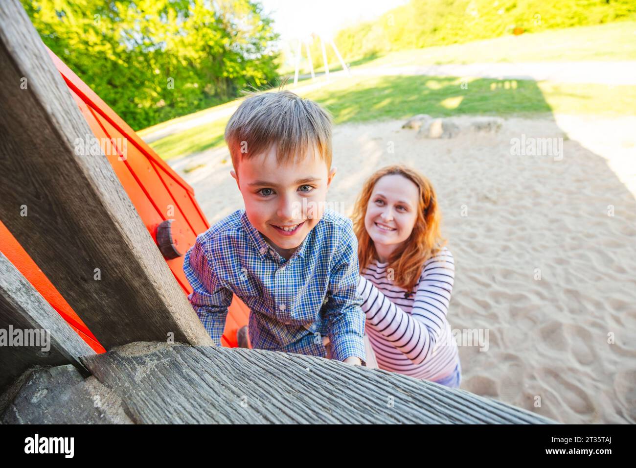 Mother helping son to climb outdoor play equipment at playground Stock Photo