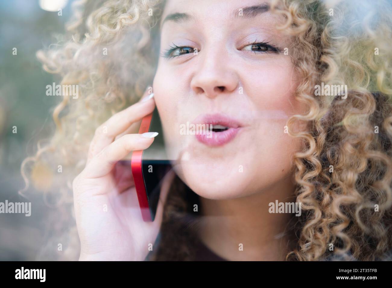 Smiling young woman with curly hair talking on phone Stock Photo