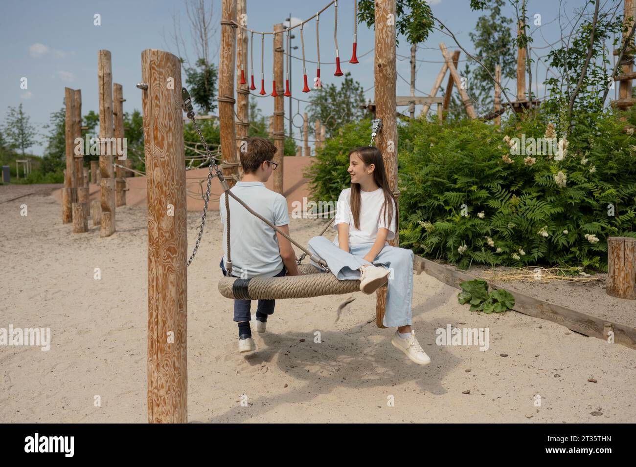Friends spending leisure time sitting on swing at playground Stock Photo