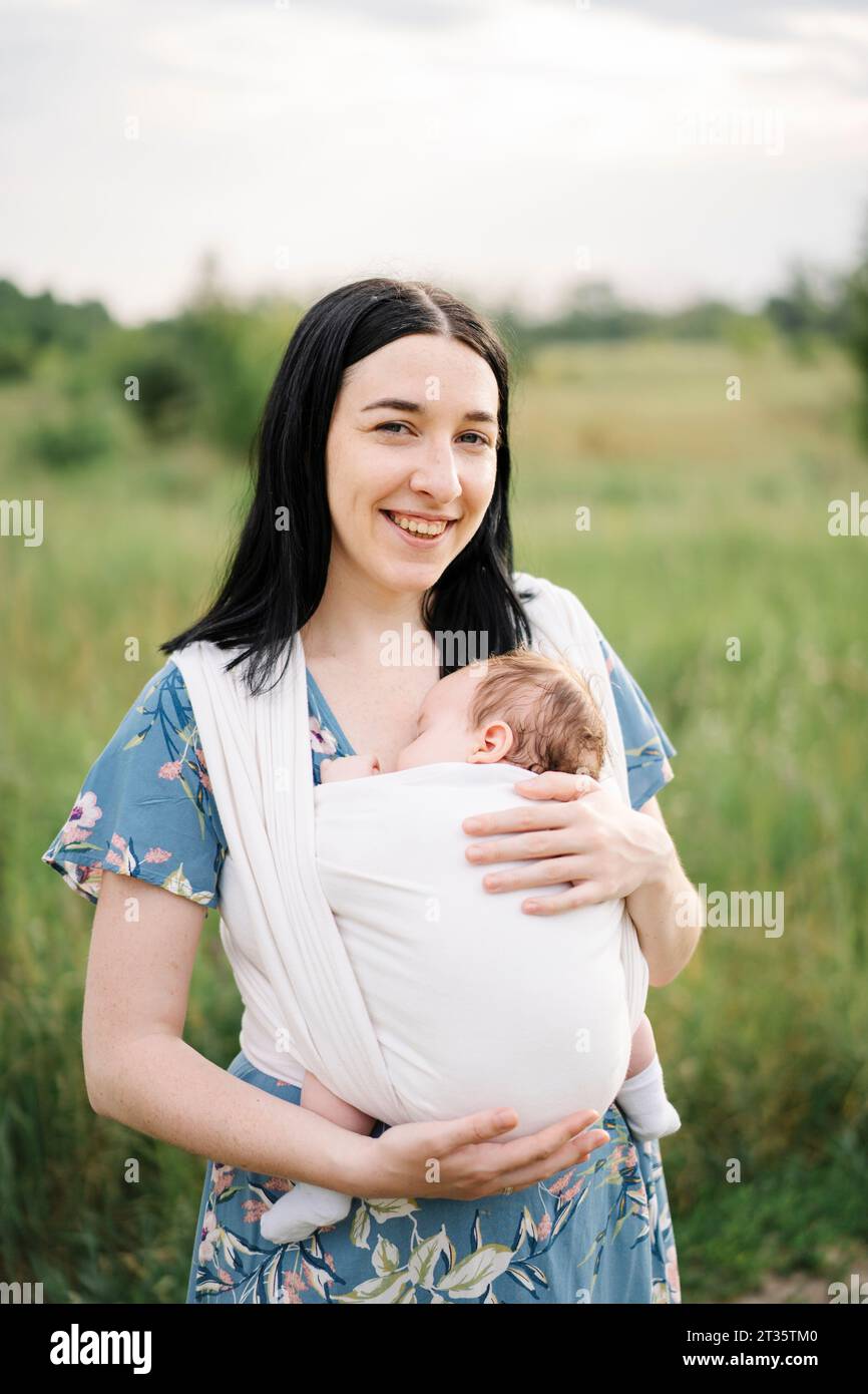 Smiling mother holding daughter wrapped in baby sling Stock Photo