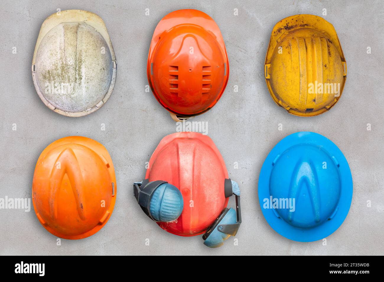 Six colorful old and worn construction helmets hanging on a concrete wall Stock Photo