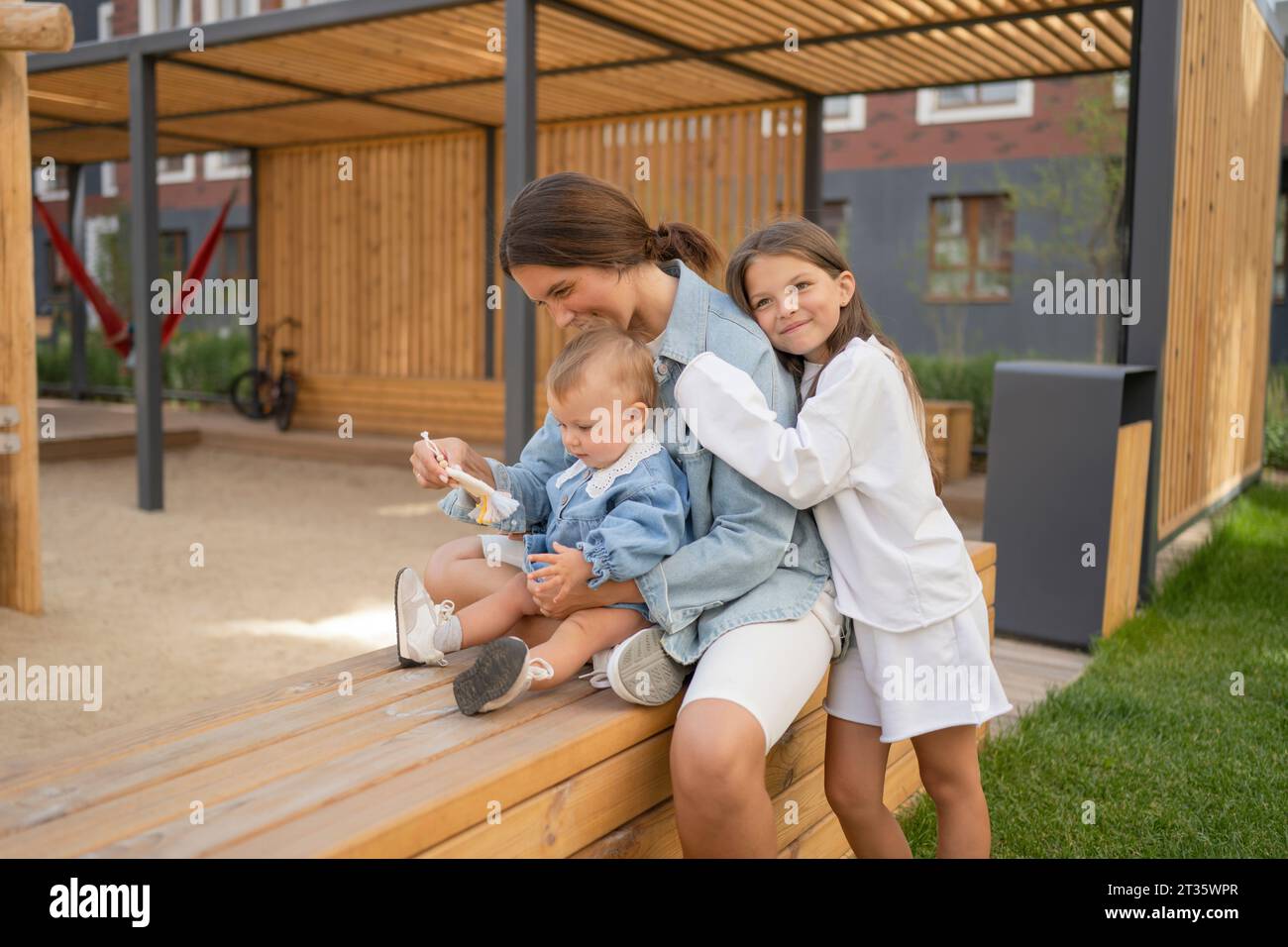 Mother with children spending leisure time on bench in back yard Stock Photo