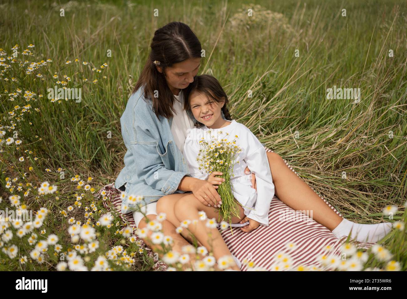 Mother and daughter sitting with bunch of daisy flowers on sunny day Stock Photo