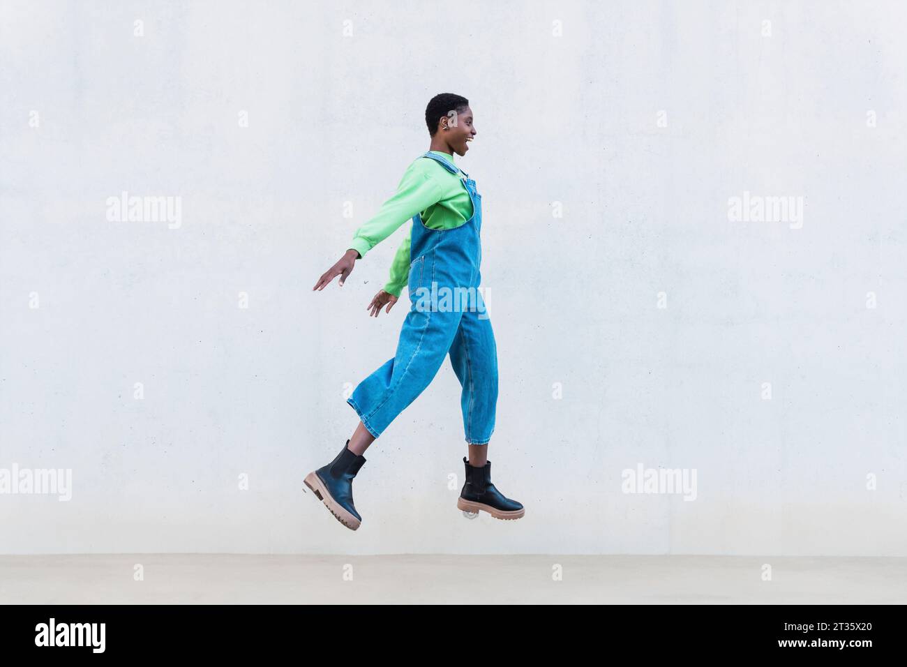 Cheerful woman jumping in front of white wall Stock Photo