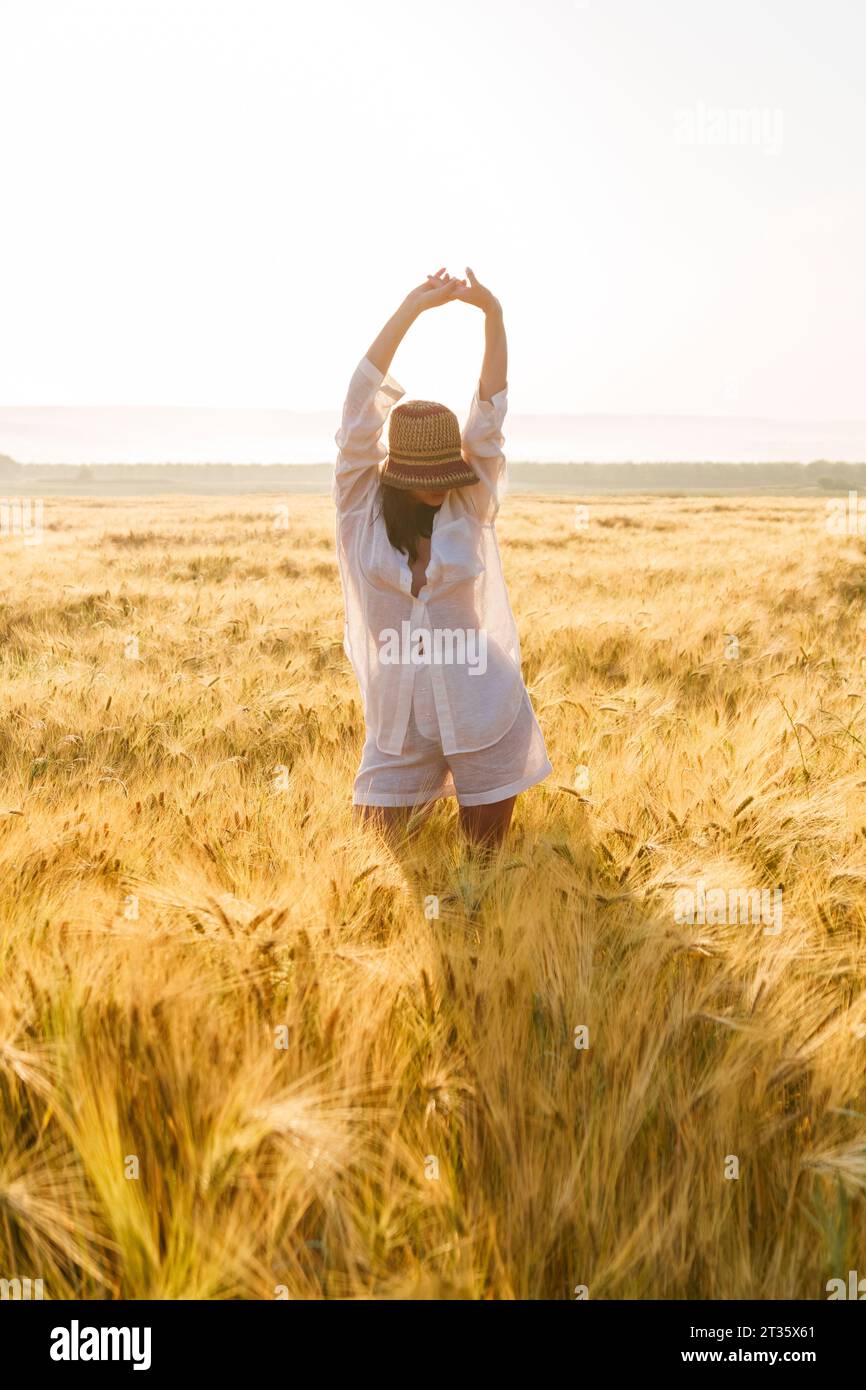 Woman with arms raised standing amidst wheat crop in field Stock Photo