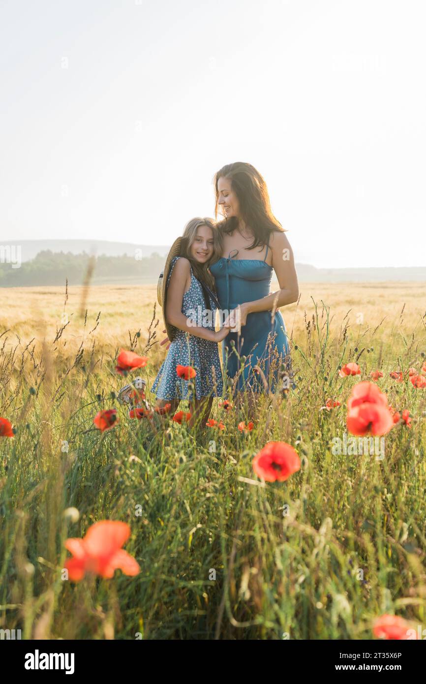 Mother and daughter embracing each other in poppy field Stock Photo