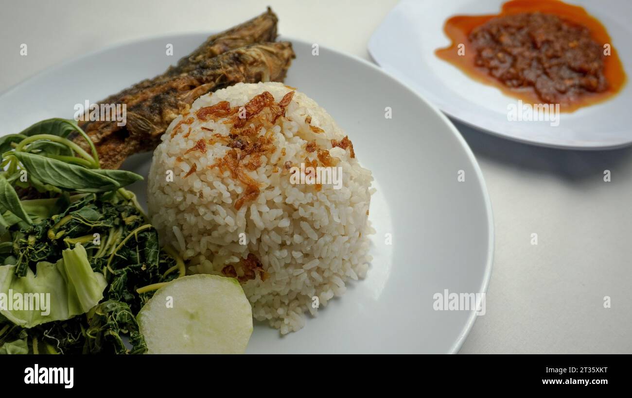 catfish pecel food containing uduk rice, fried catfish, boiled papaya leaves, raw cabbage and basil leaves and chili sauce Stock Photo