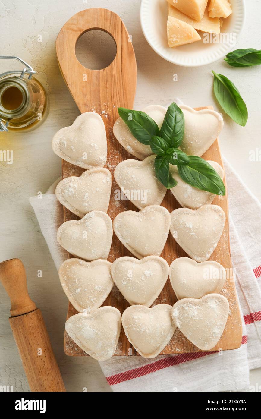 Italian ravioli pasta in heart shape. Tasty raw ravioli with flour and basil on white background. Food cooking ingredients background. Valentines or M Stock Photo