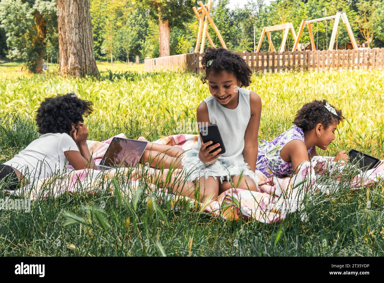 Happy sisters spending time with wireless technology in garden Stock Photo