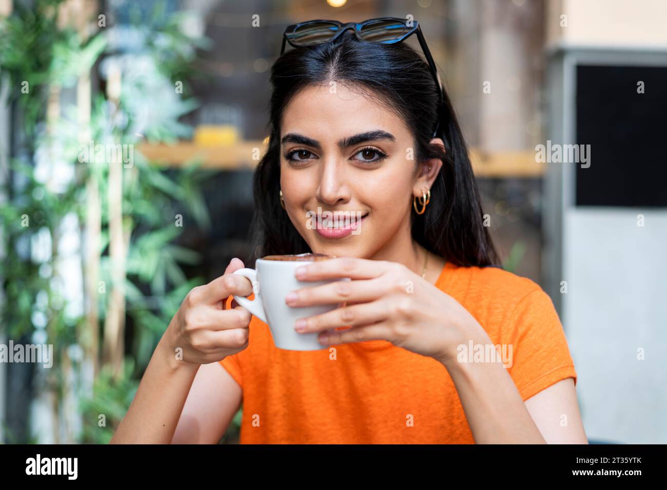 Smiling young woman enjoying coffee at cafe Stock Photo