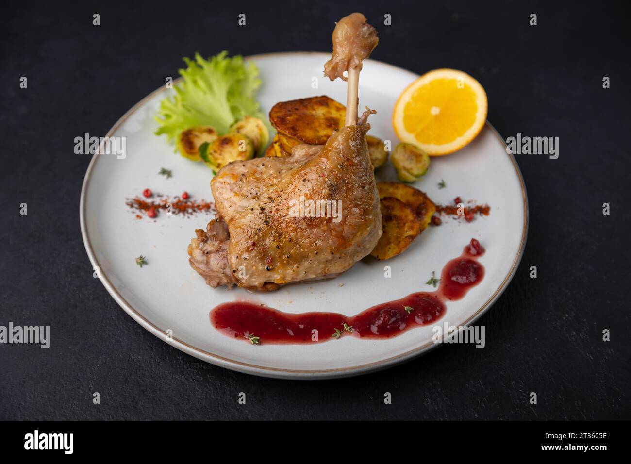 Duck leg confit with Brussels sprouts, baked potatoes, thyme, orange and lingonberry sauce. Traditional French cuisine. Selective focus, close-up, bla Stock Photo