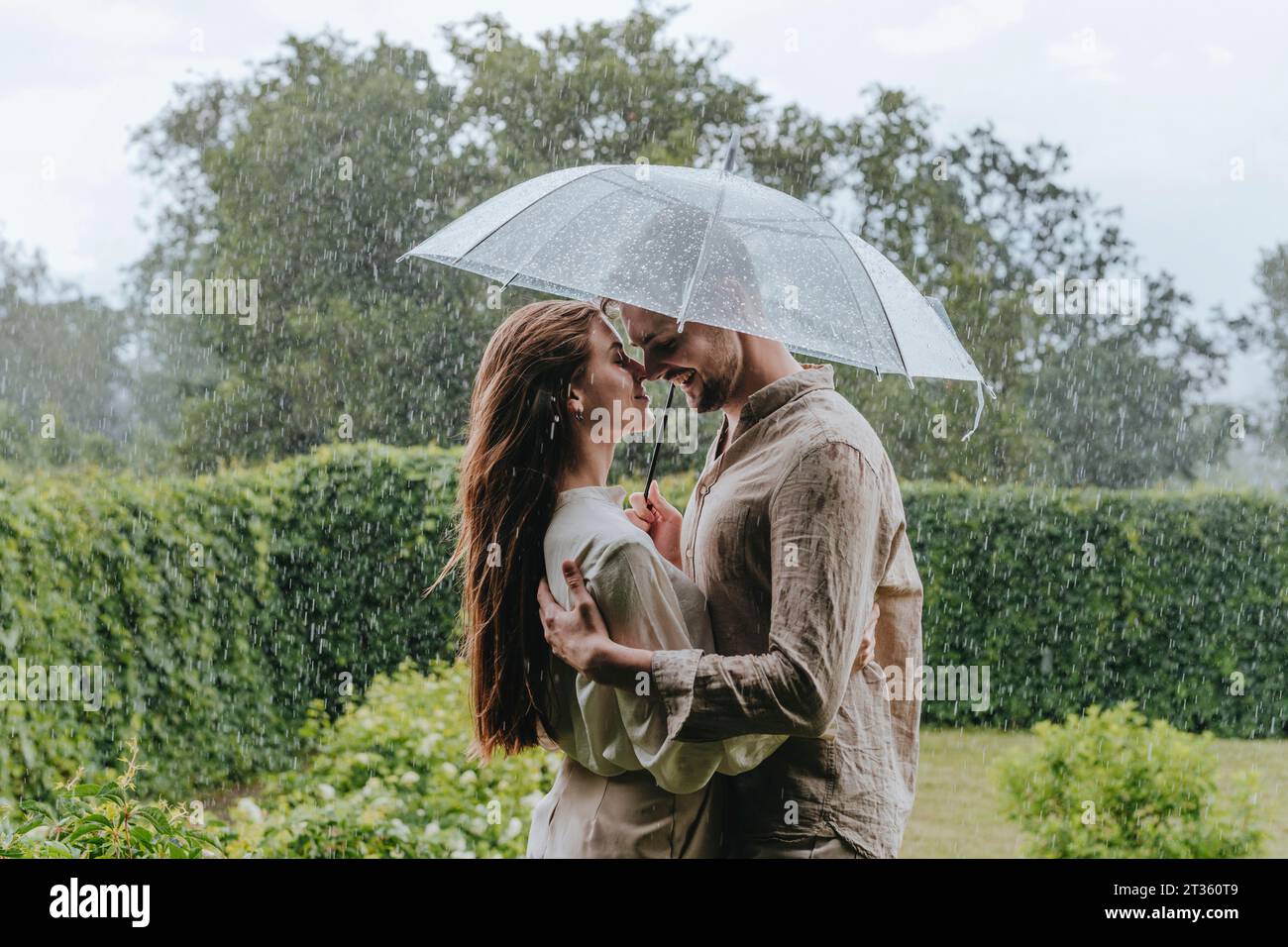 Romantic couple standing with umbrella in rain at garden Stock Photo ...