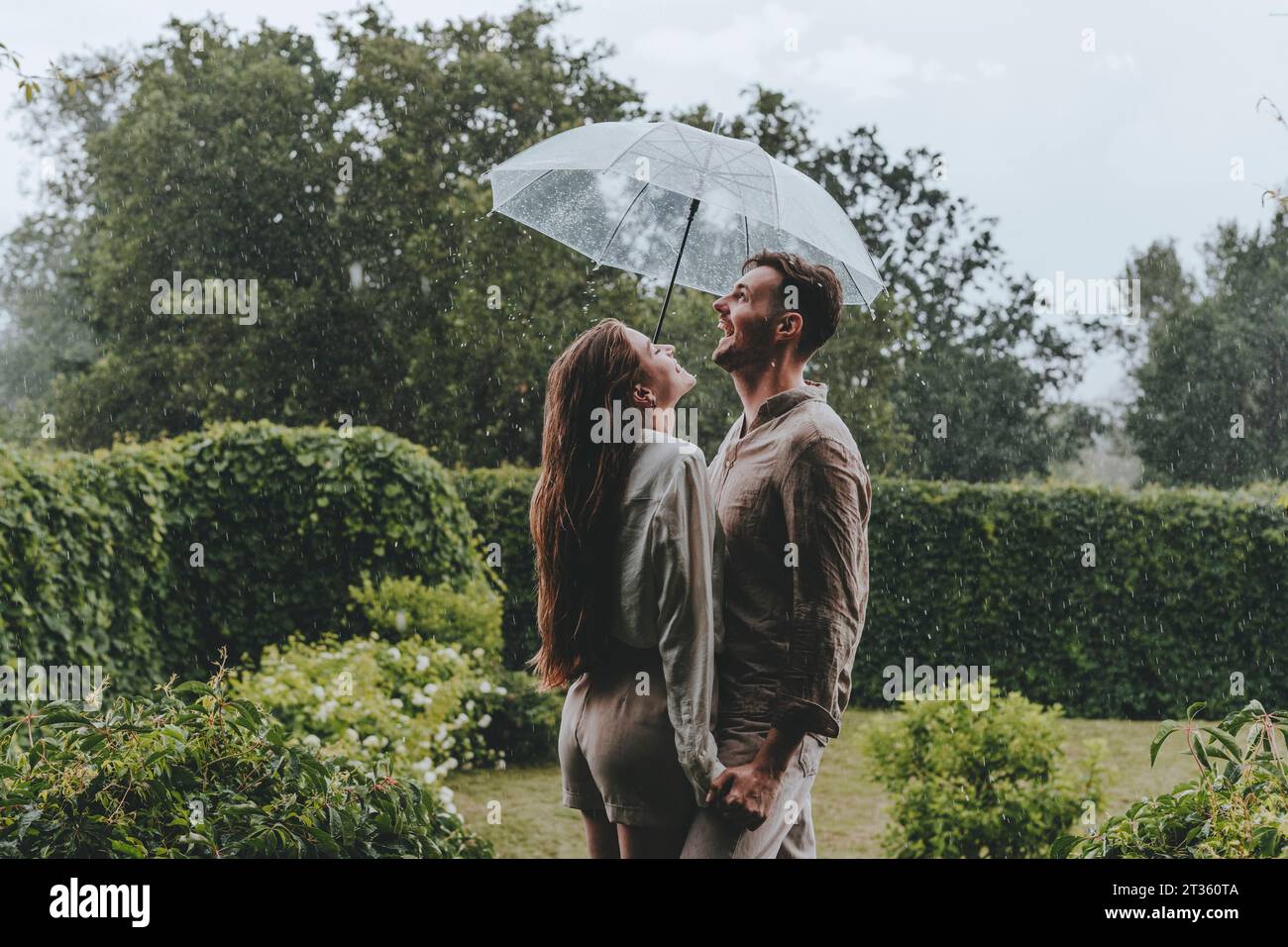 Happy couple holding umbrella and enjoying in rain at garden Stock Photo