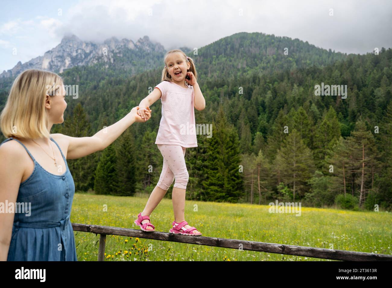 Woman holding daughter's hand walking on railing in front of mountains Stock Photo