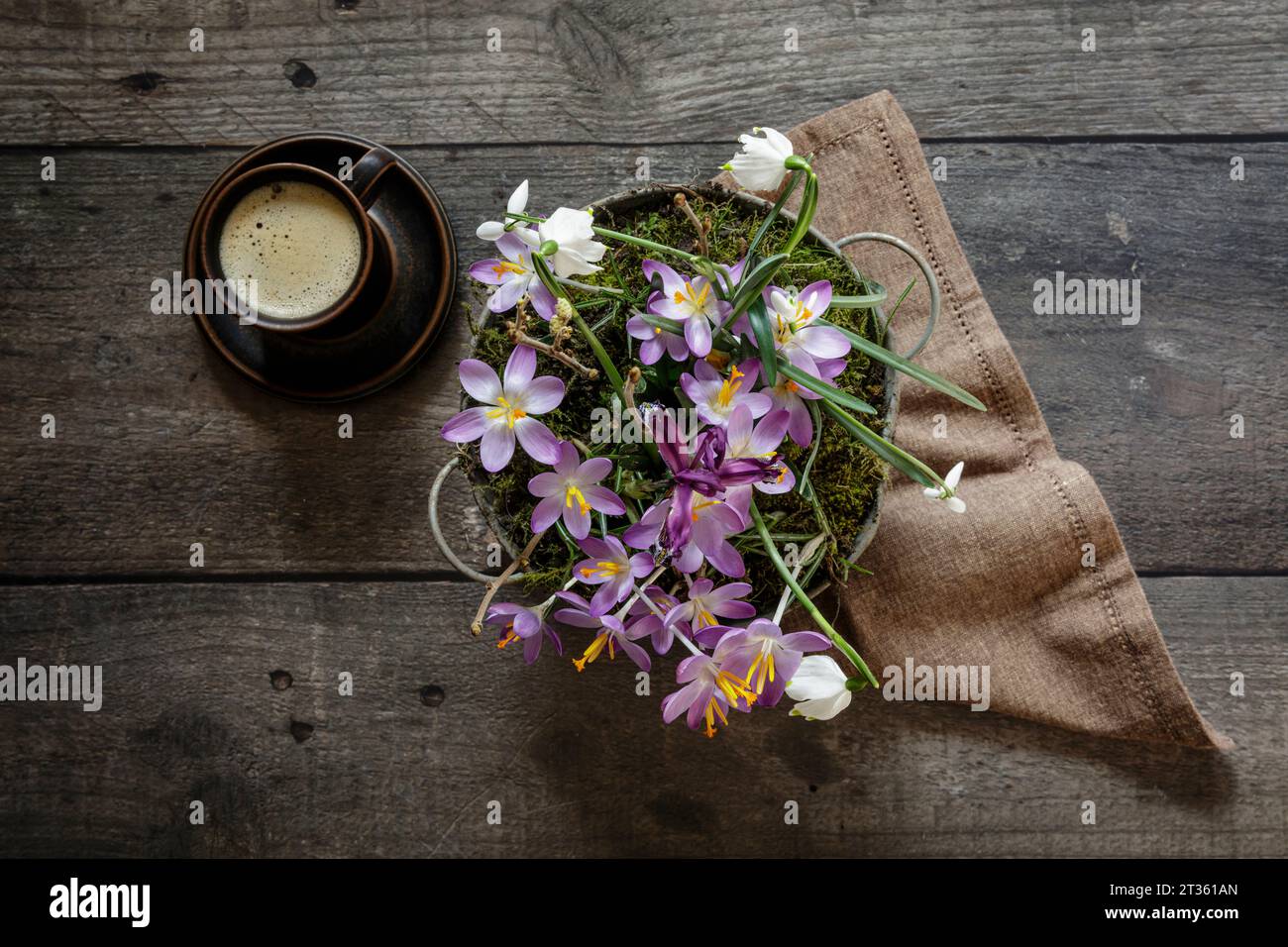 Cup of coffee and springtime flowers in metal bucket standing on wooden table Stock Photo