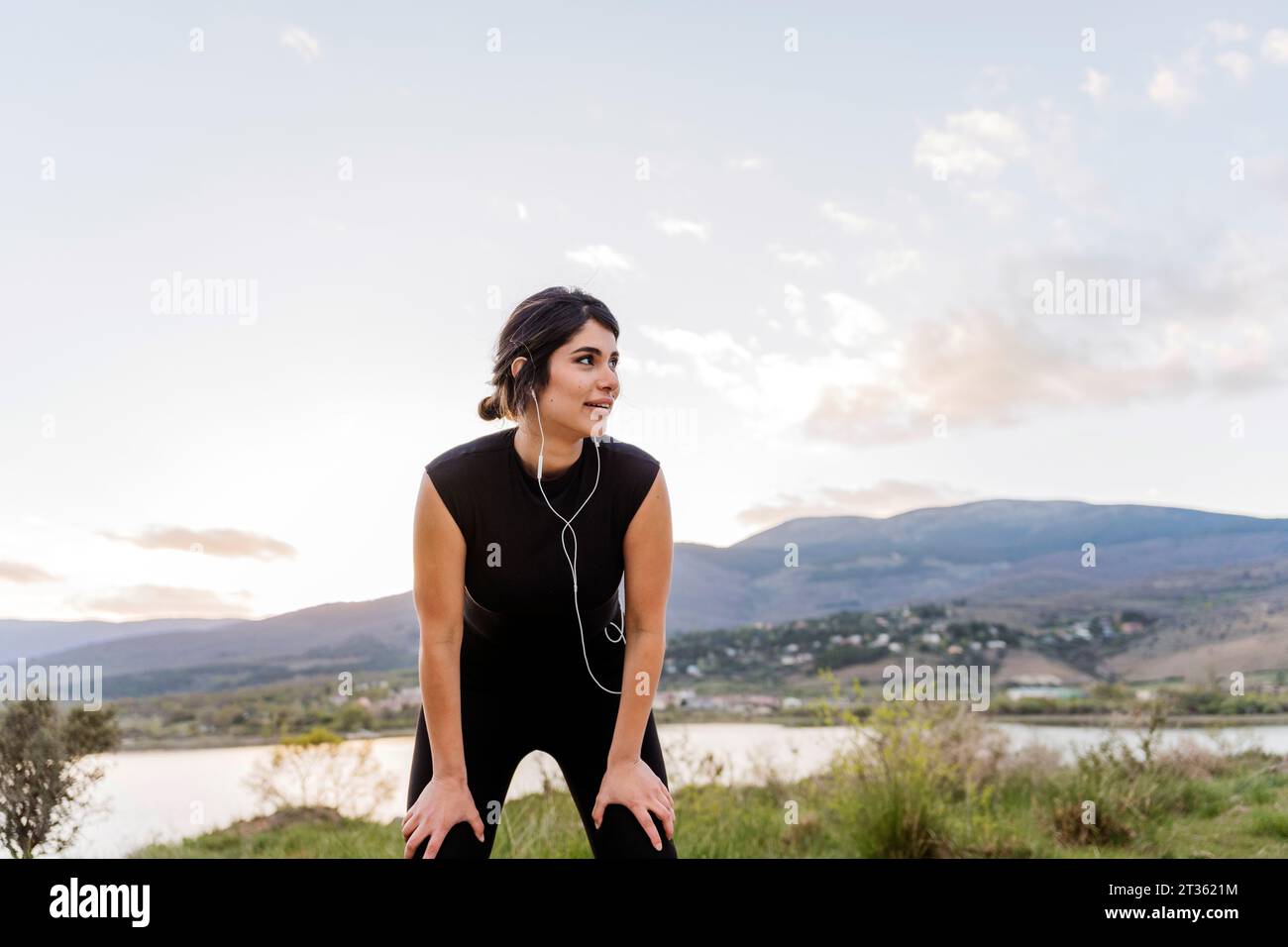 Contemplative woman with hands on knee in front of mountains Stock Photo