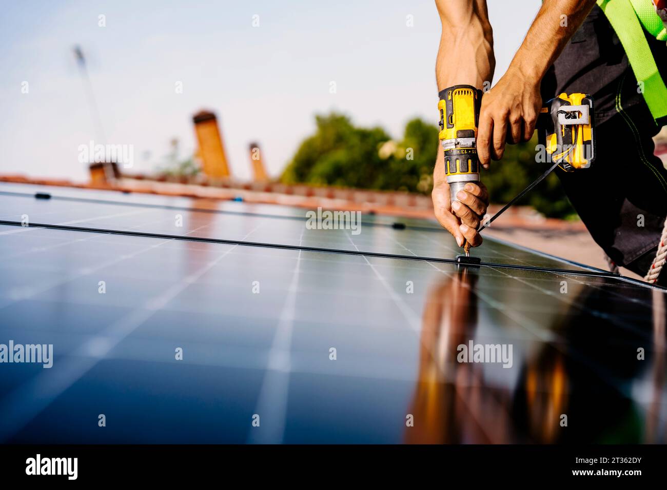 Hands of engineer with drill machine installing solar panels Stock Photo