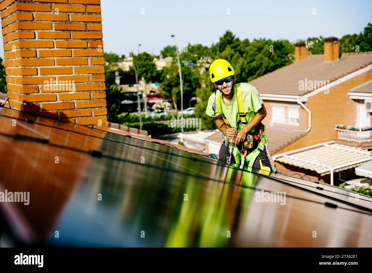 Happy engineer with drill machine installing solar panels on roof Stock Photo