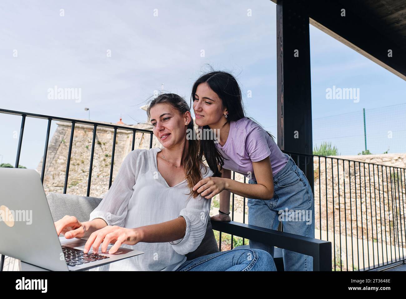 Two young women using laptop on balcony Stock Photo