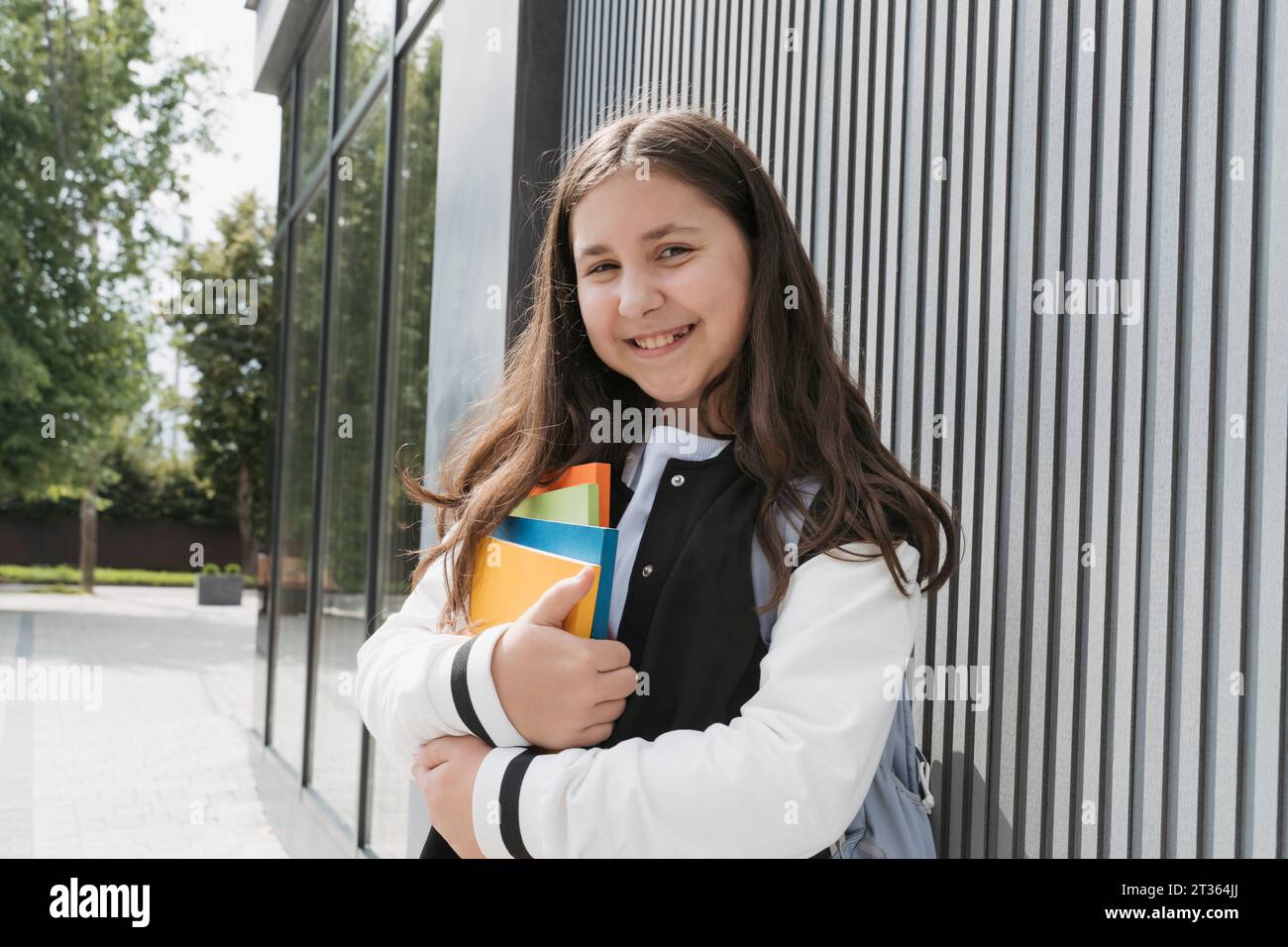 Smiling schoolgirl holding books near school building Stock Photo - Alamy