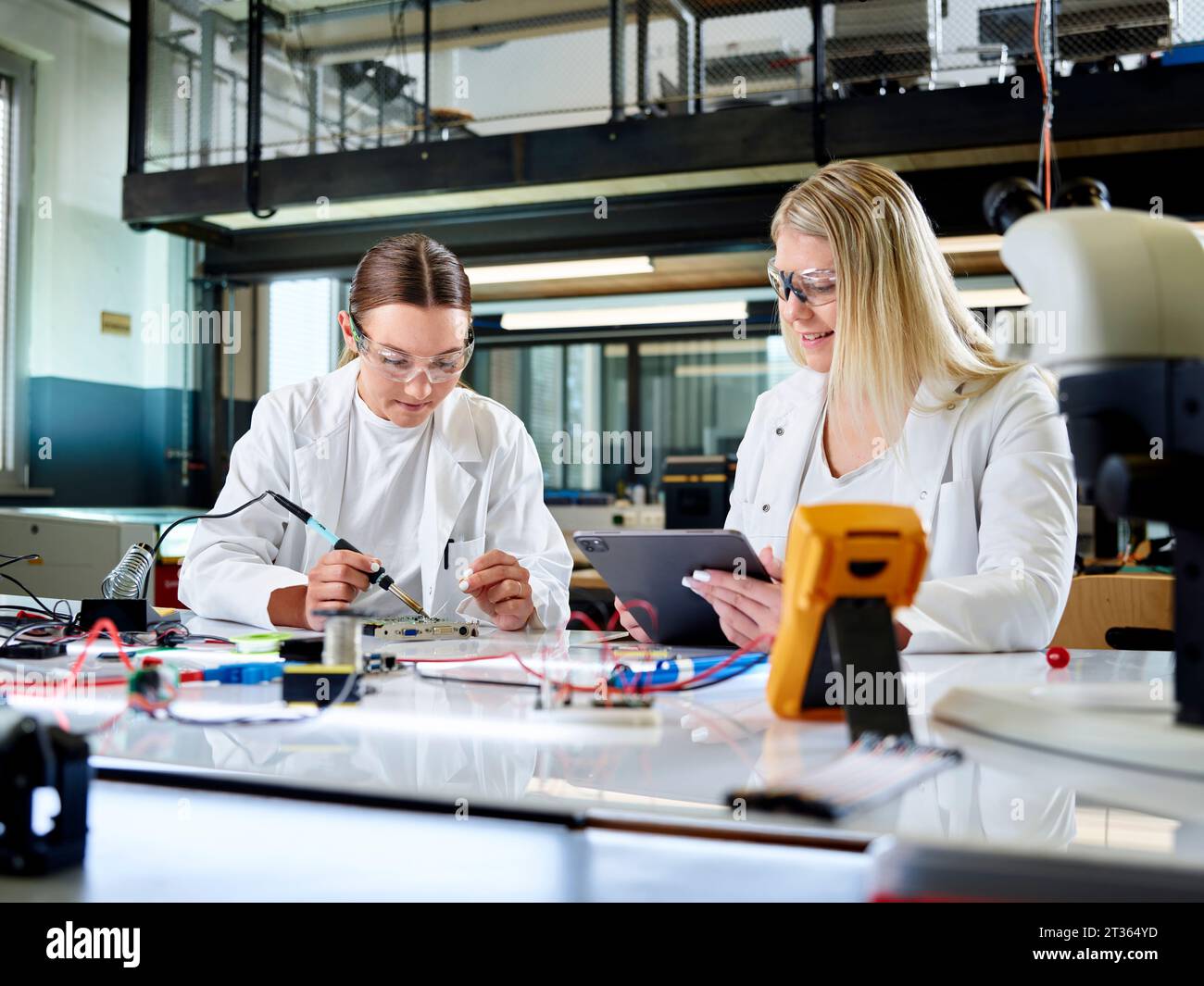 Smiling scientist measuring circuit board with colleague using tablet PC Stock Photo