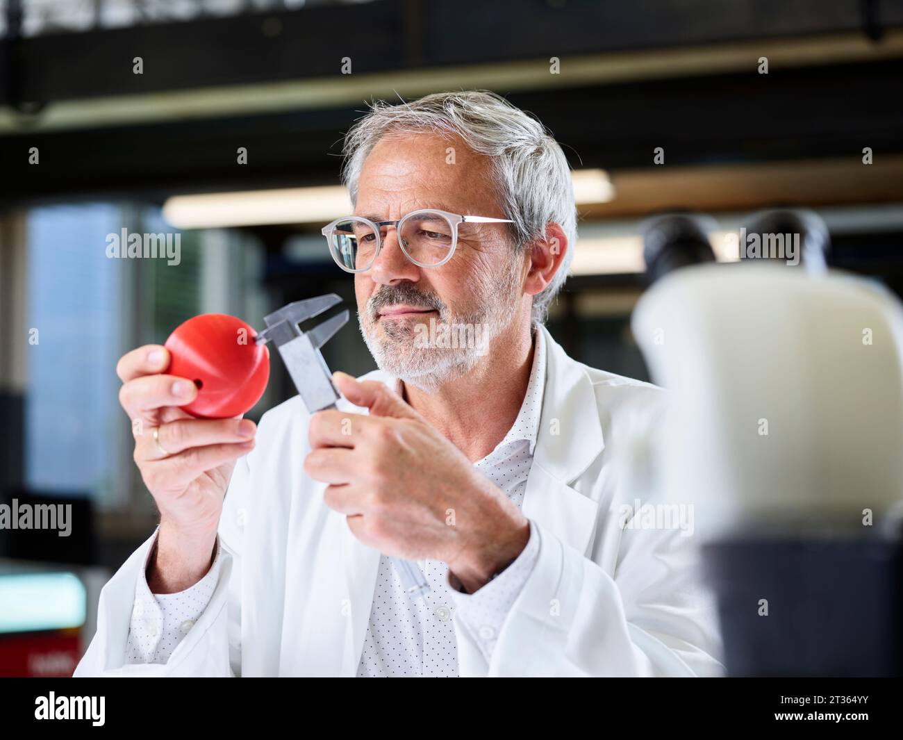 Scientist measuring red ball with caliper in laboratory Stock Photo
