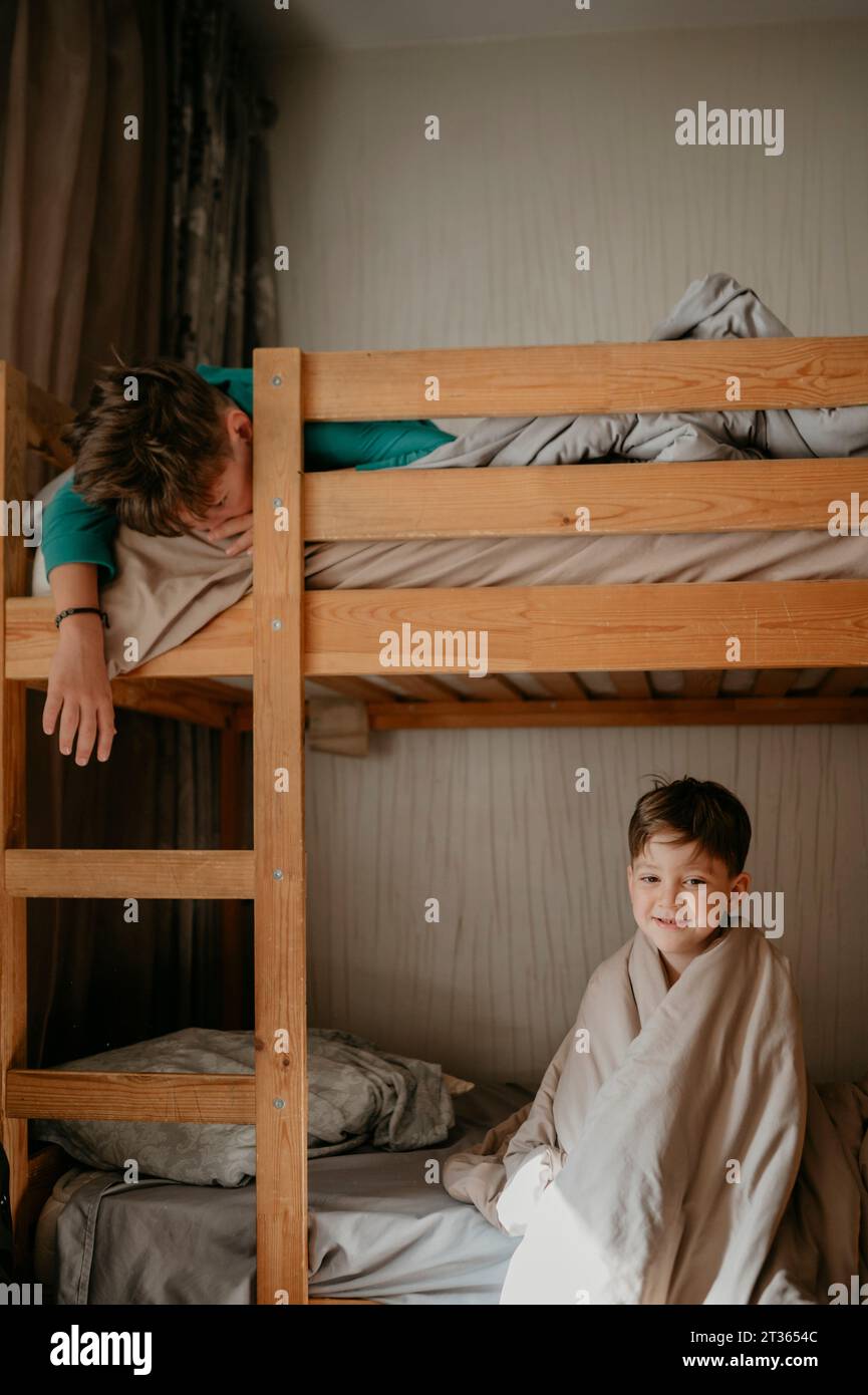Smiling boy sitting with brother lying on bunkbed Stock Photo