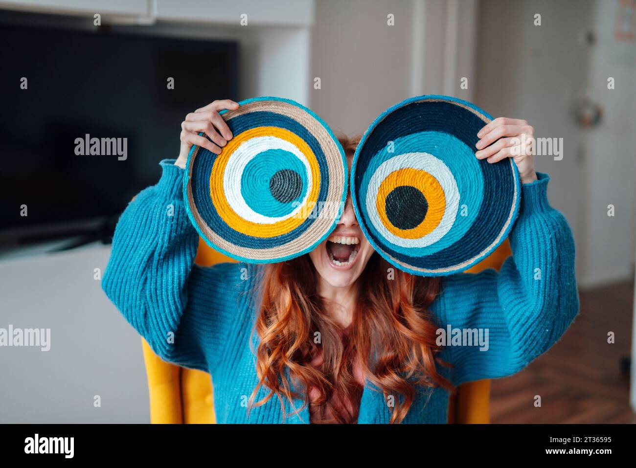 Happy woman holding macrame evil eyes over face at home Stock Photo