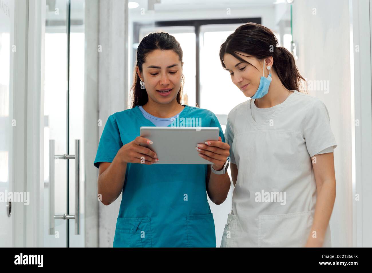 Smiling dentist using tablet PC by colleague in corridor Stock Photo