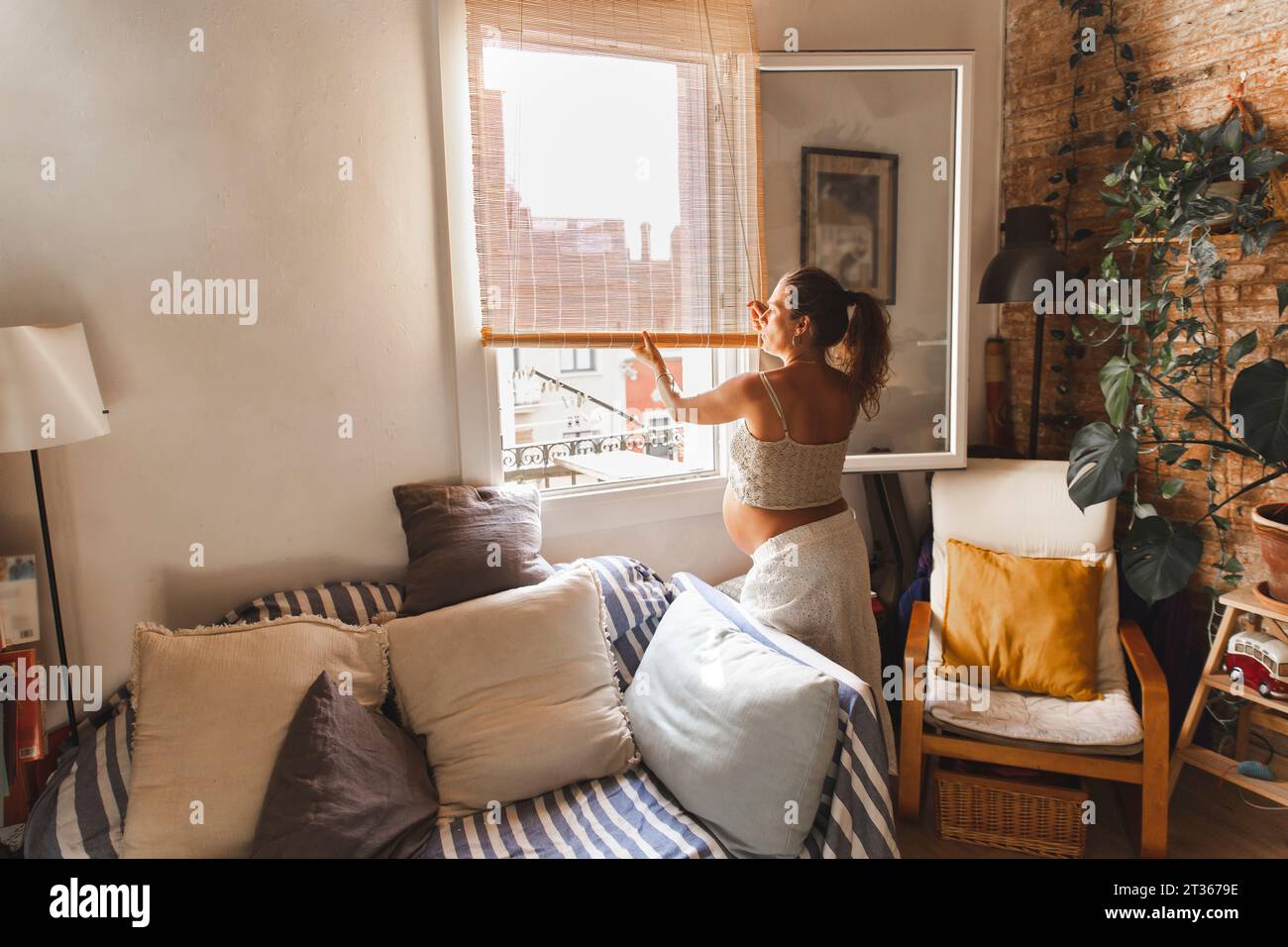 Pregnant woman closing window blinds at home Stock Photo