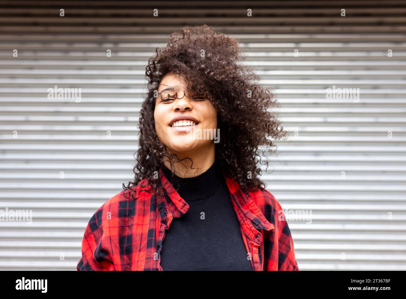 Smiling woman with curly hair in front of shutter Stock Photo