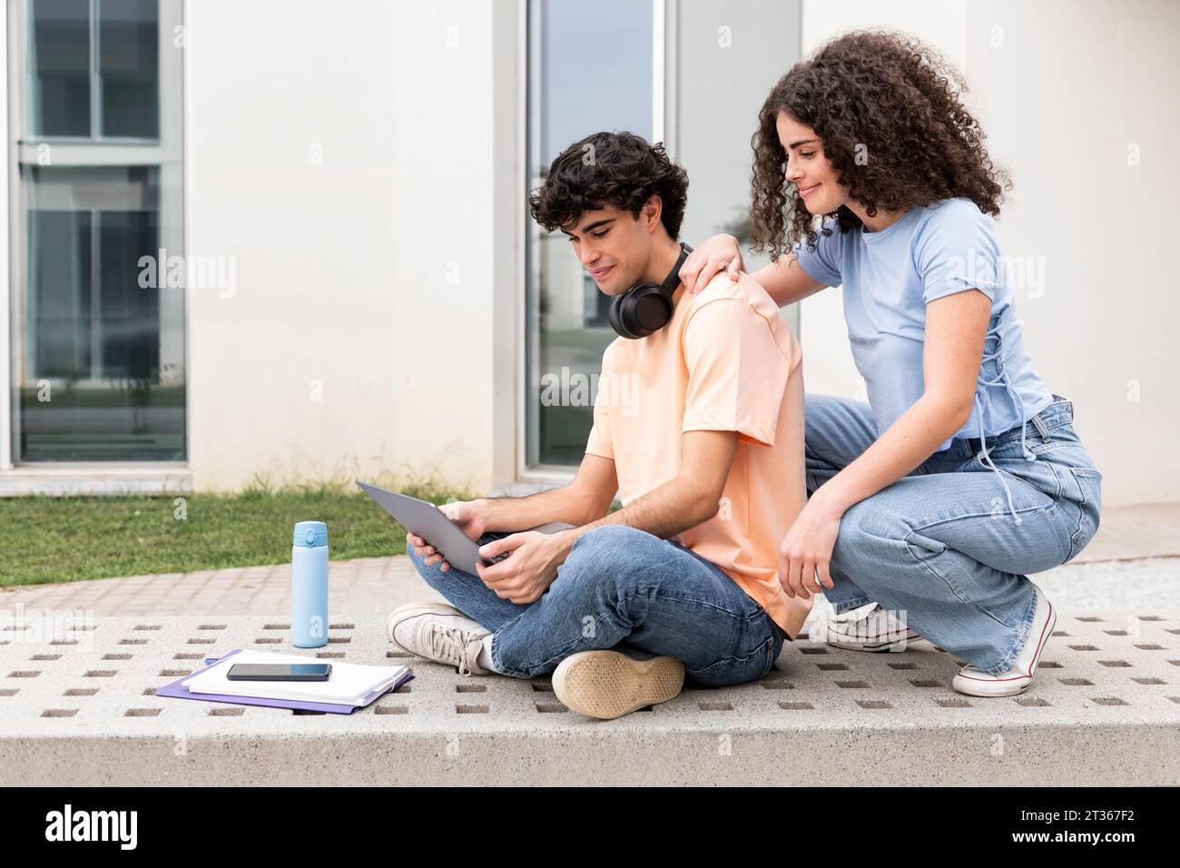 Smiling students using laptop on concrete bench in campus Stock Photo
