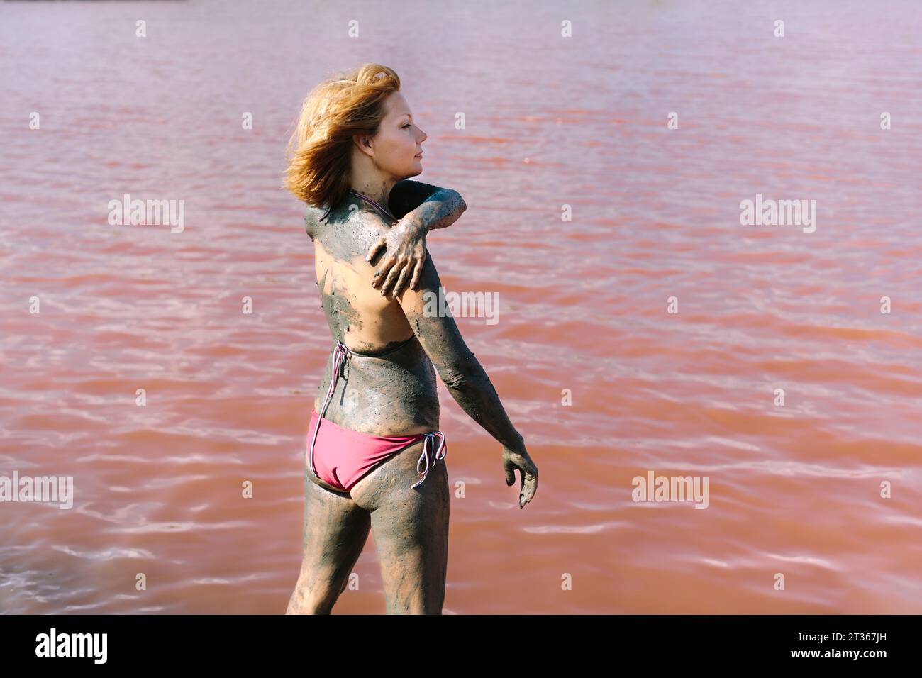 Carefree woman applying mud on skin near lake Stock Photo