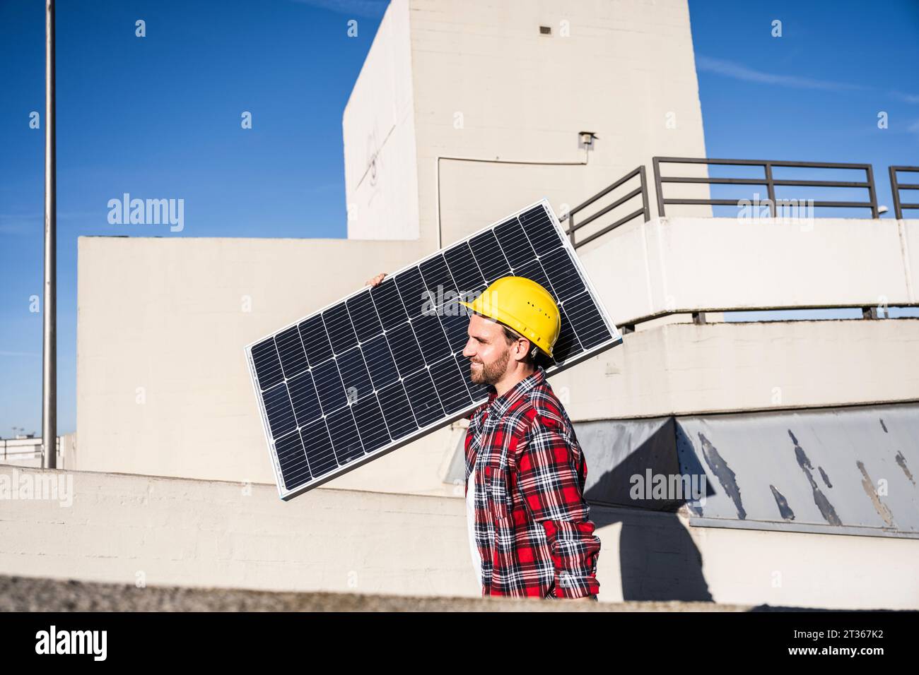 Engineer wearing hardhat carrying solar panel on shoulder Stock Photo