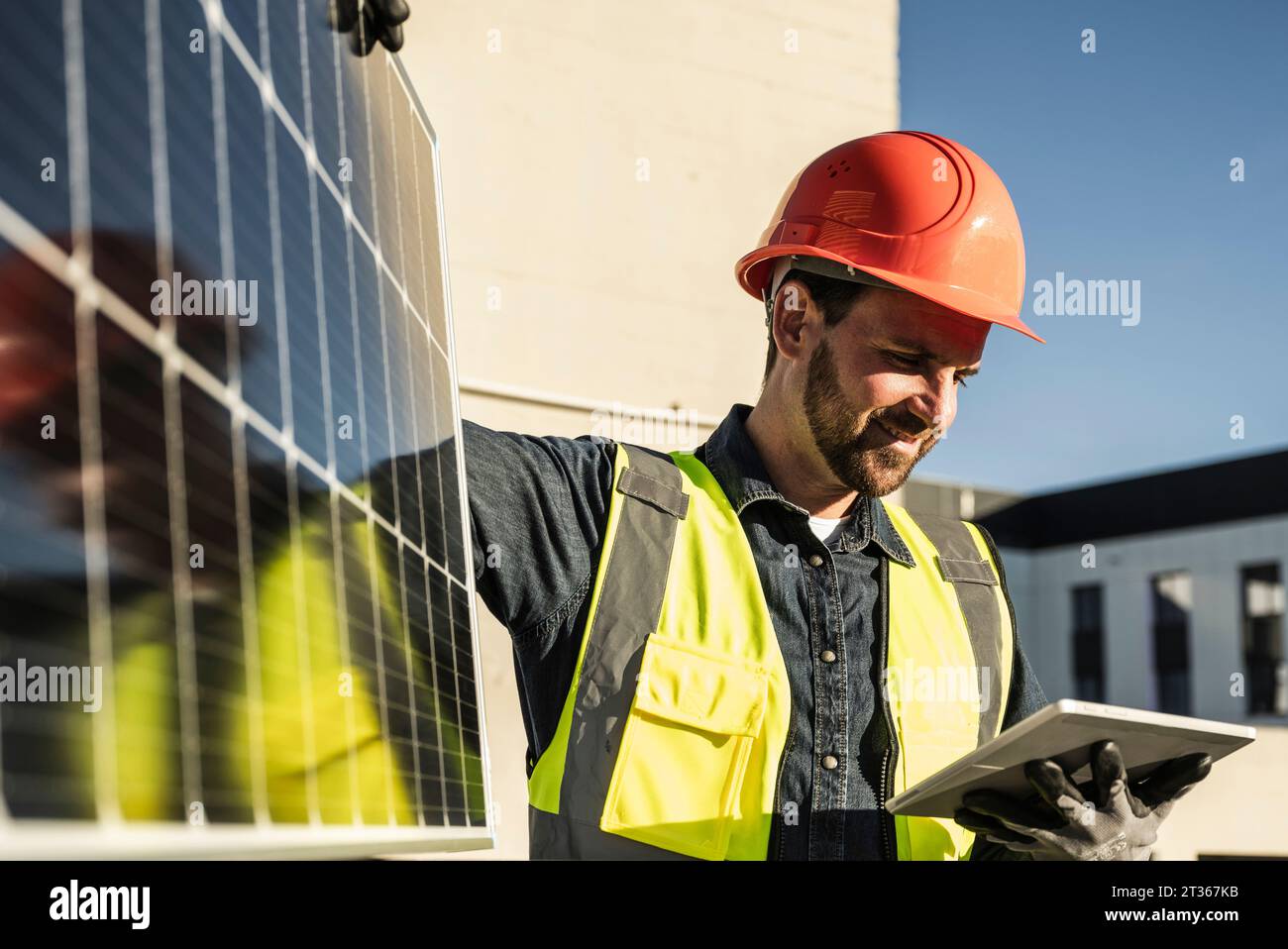 Smiling engineer wearing protective workwear using digital tablet by solar panel Stock Photo